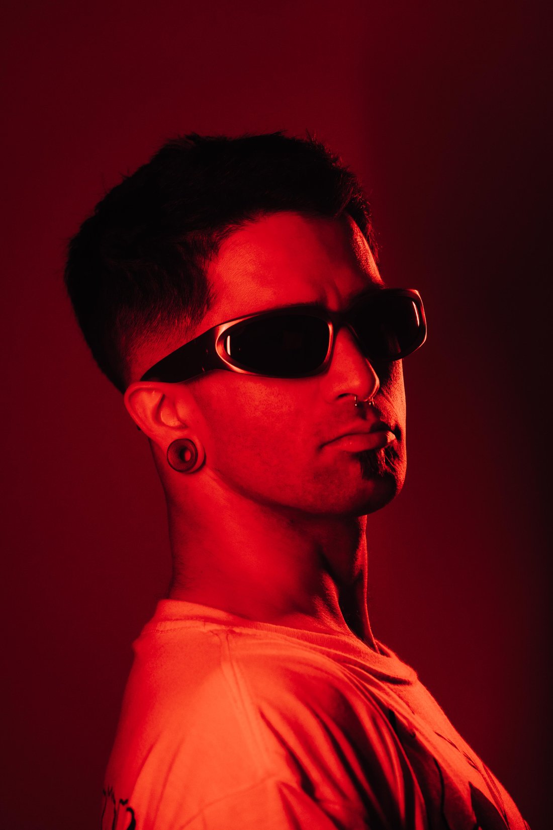 Retrato de perfil de Diego Amaro con lentes de sol, sobre fondo rojo
